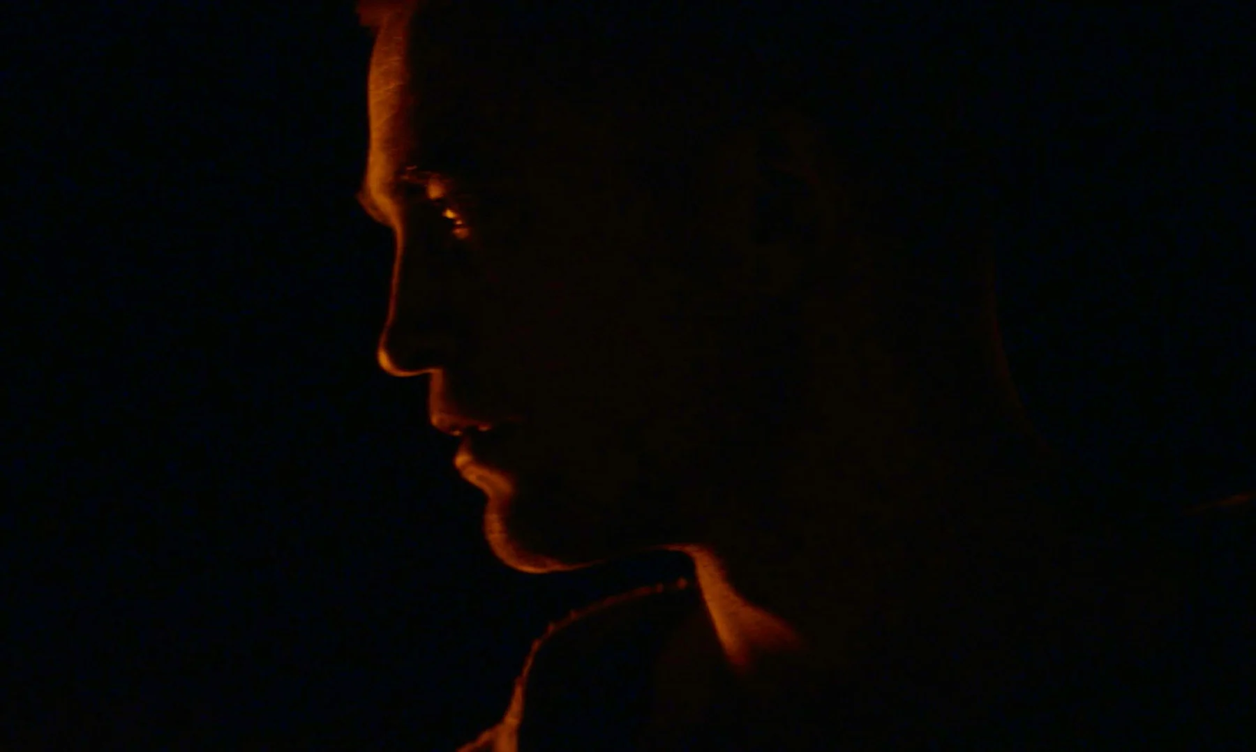 A man’s profile catches a narrow edge of warm orange light.