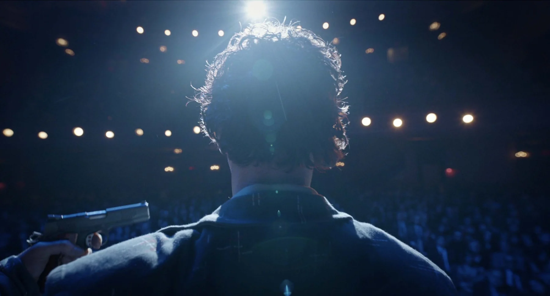 An actor stands onstage with a gun against his head.