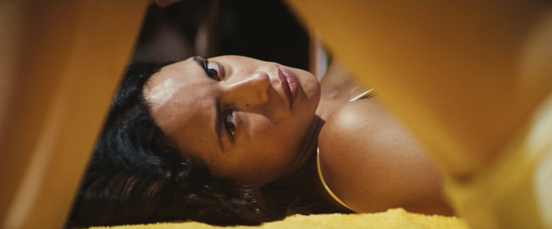 A woman reclines in warm yellow light, her face partly in shadow.
