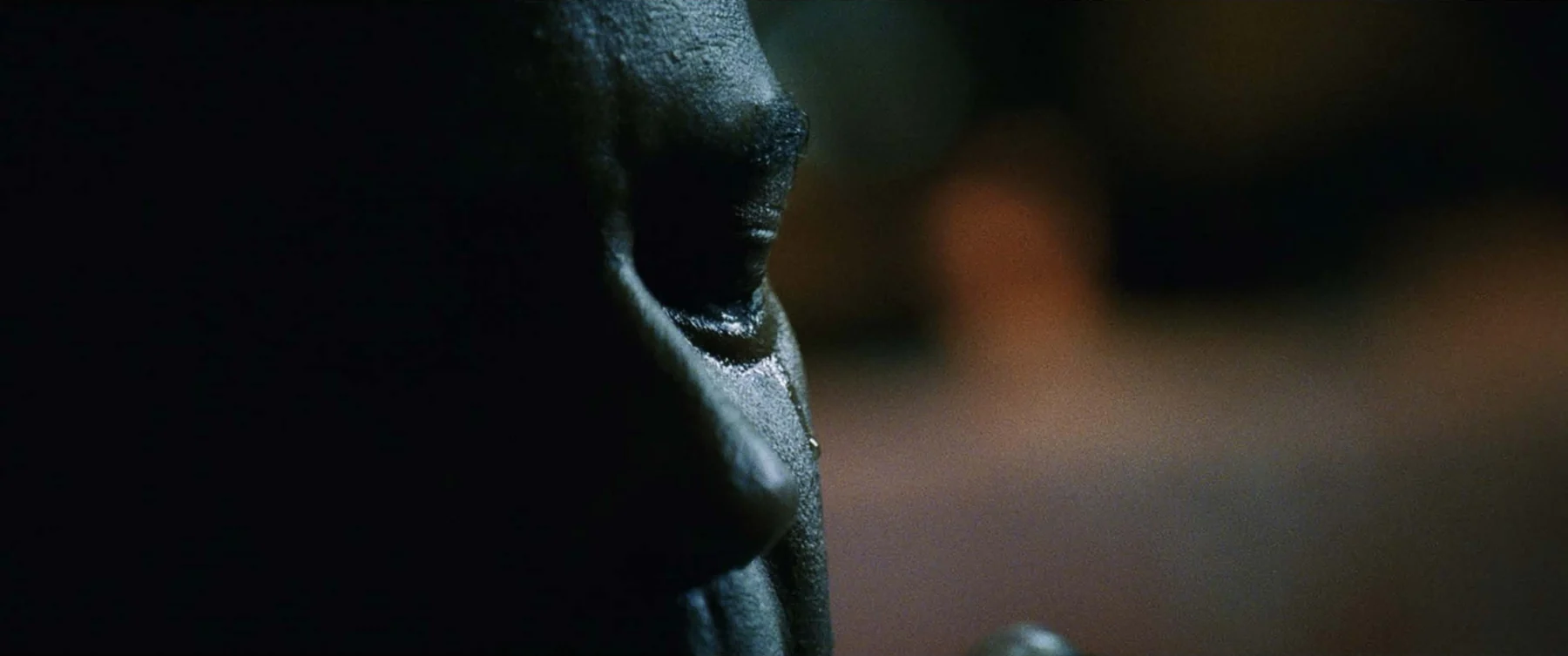 An extreme close-up of a man’s face in shadow, edged with cool light.