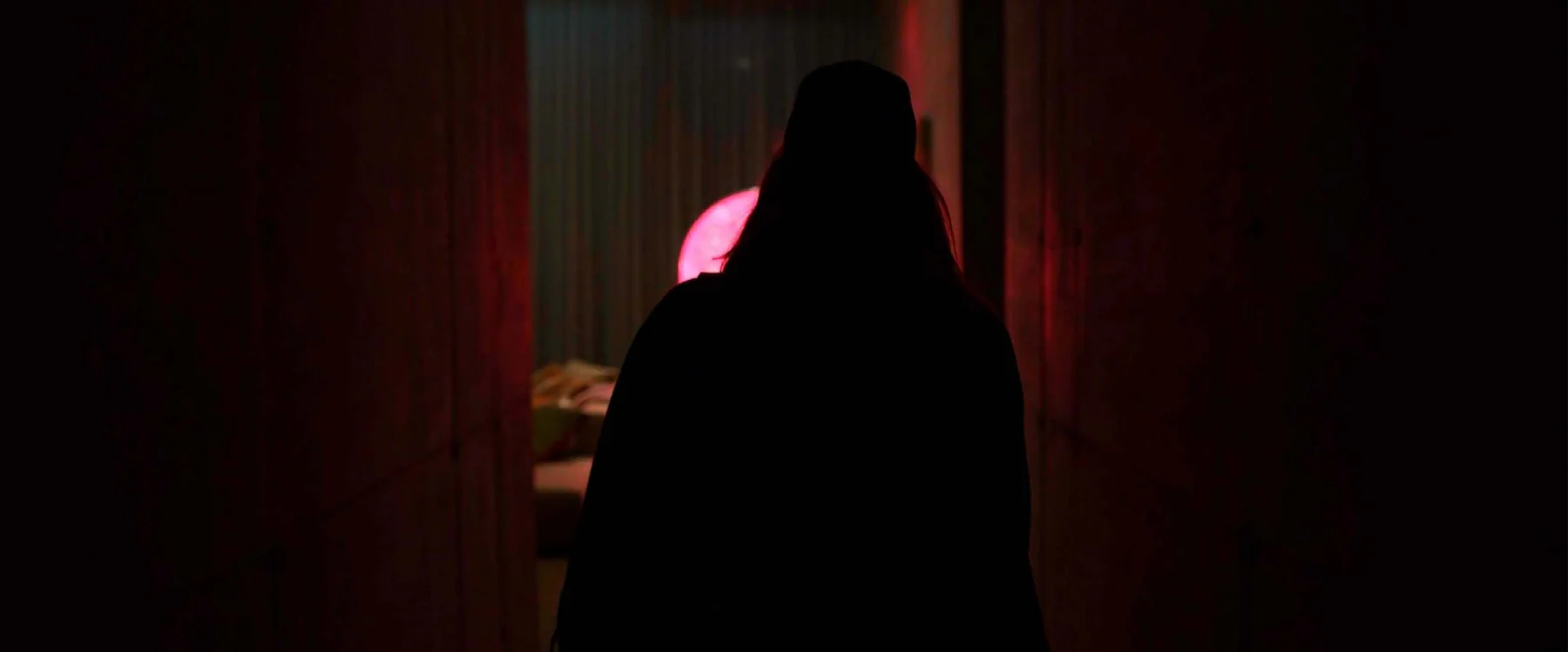 A woman’s silhouette is framed by red curtains and a glowing pink light.