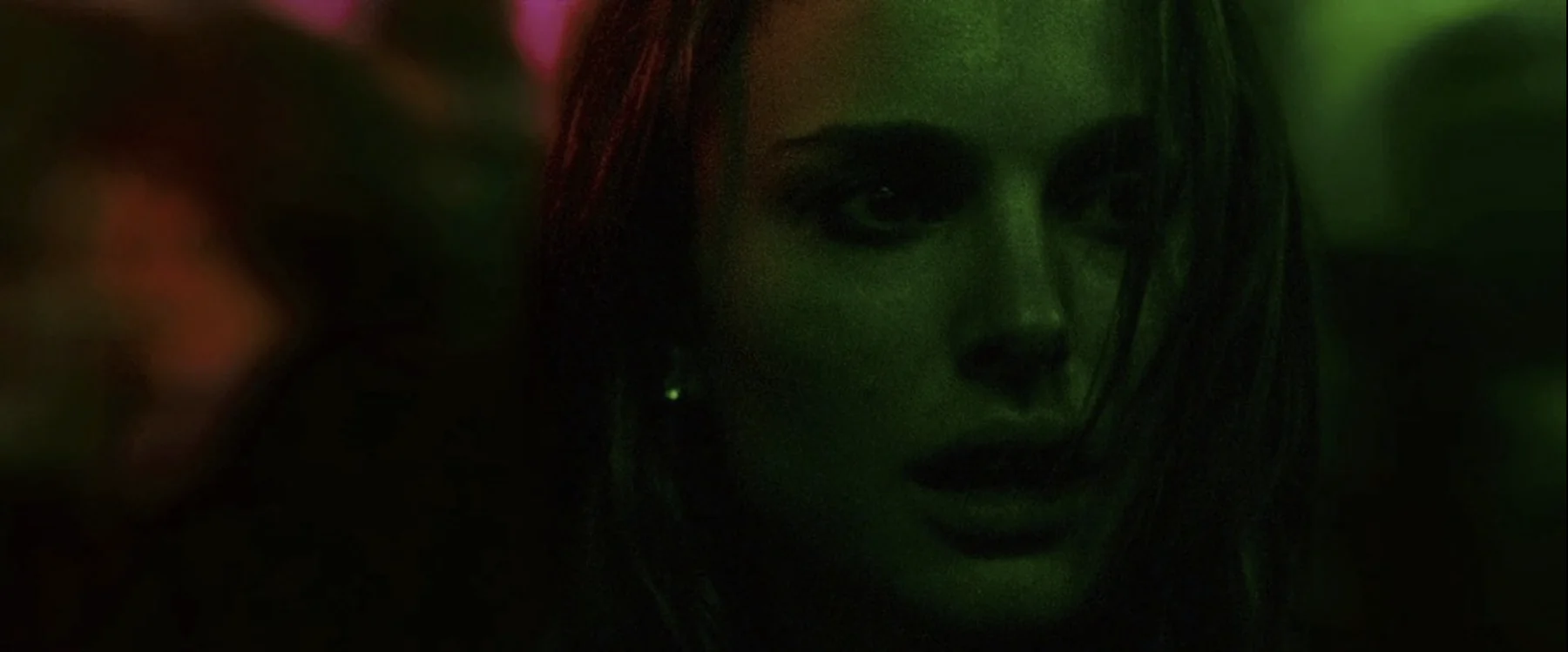 A woman’s face is caught in green light with magenta reflections.