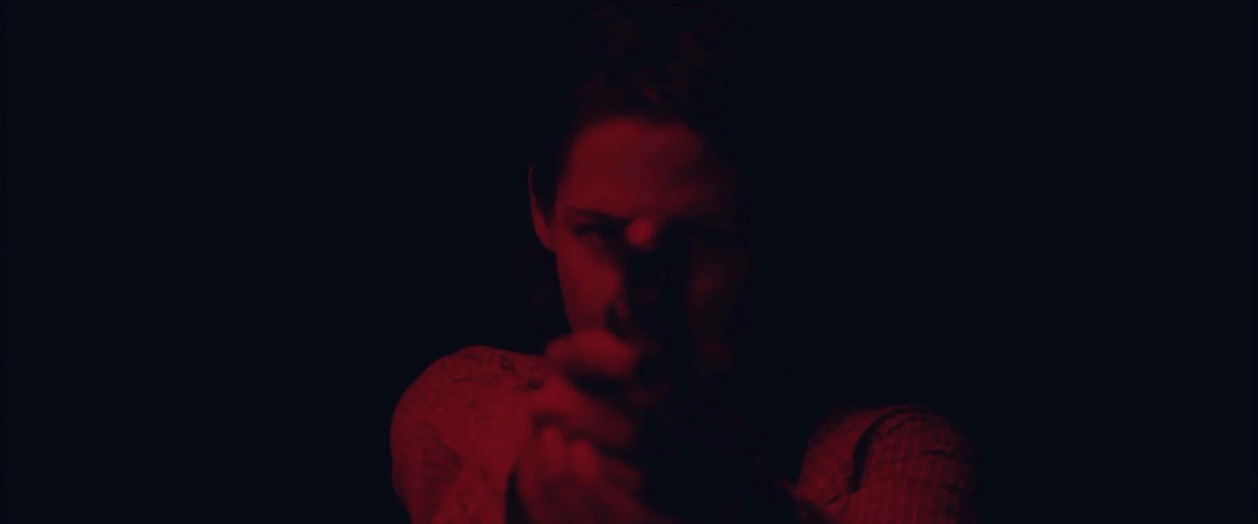 A woman aims a gun under red light.